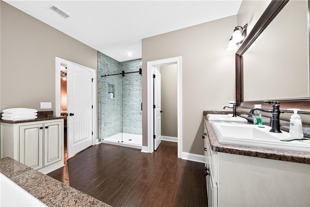 611 Padgetts Road Opelika, AL 36804 - Photo 30 of 64 Dual vanity with granite countertops, wood-finish flooring, glass-enclosed shower with brick-look tile, and white cabinetry