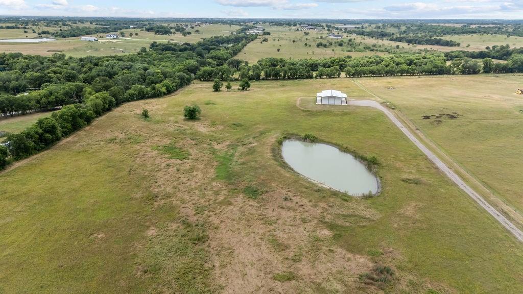 1161 Alsdorf Road Ennis, TX 75119 - Photo 6 of 28 Expansive acreage featuring a private pond, a functional white barn, a long gravel driveway, and a perimeter of mature trees