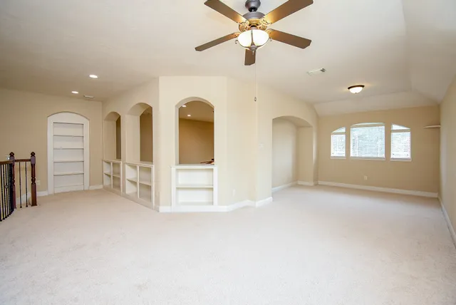 an empty room with chandelier fan and windows
