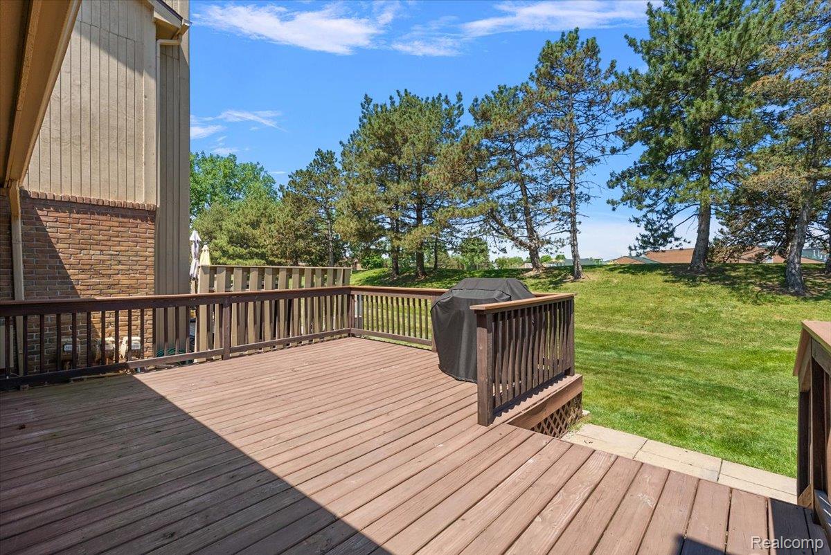 552 Tennyson Rochester, MI 48307 - Photo 31 of 36 Spacious outdoor deck with wood railing, featuring a large grassy area and mature evergreen trees