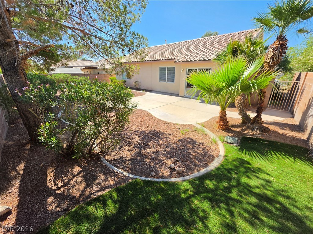 1154 Point Success Avenue Henderson, NV 89014 - Photo 2 of 26 A neatly landscaped backyard features vibrant green grass and mature palm trees alongside a private patio area.