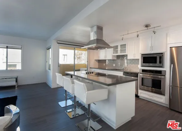 a kitchen with stainless steel appliances a sink a stove a refrigerator cabinets and a dining table with wooden floor