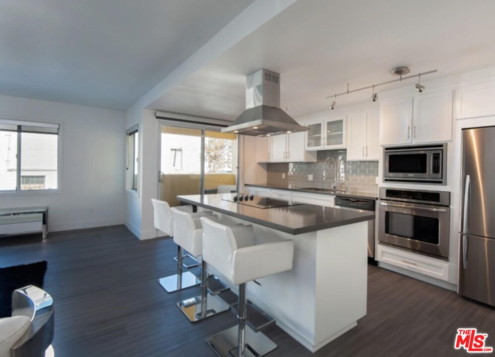 a kitchen with stainless steel appliances a sink a stove a refrigerator cabinets and a dining table with wooden floor