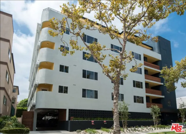 a front view of a multi story residential apartment building with yard and parking