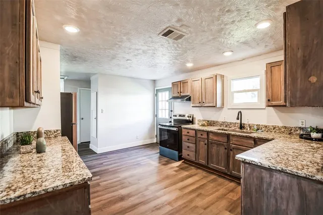 a kitchen with stainless steel appliances granite countertop hardwood floor sink stove and granite counter top