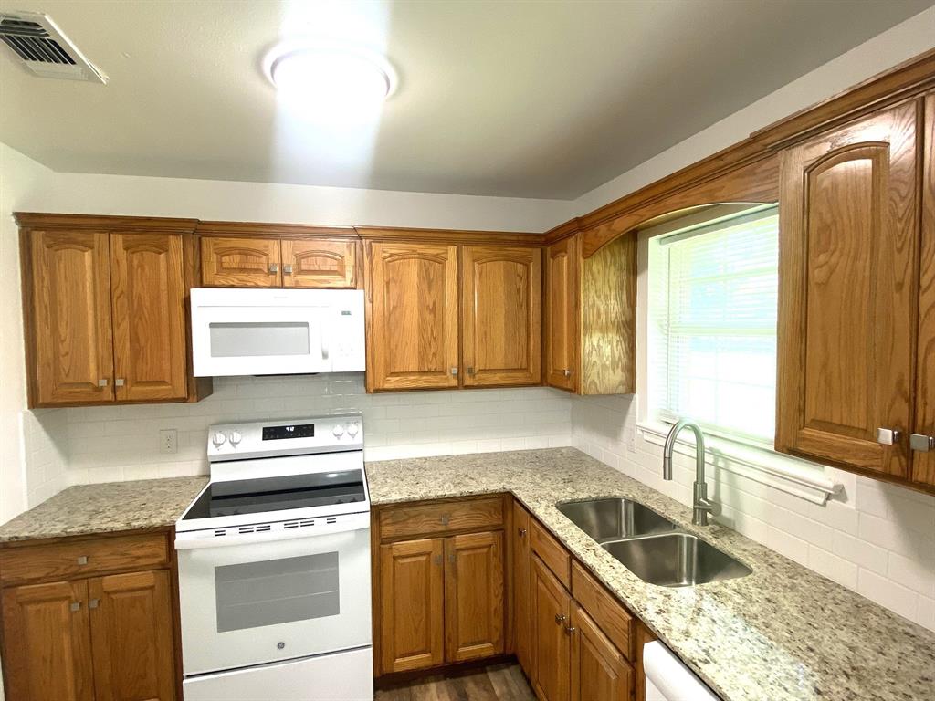 505 Red Springs Avenue Mount Pleasant, TX 75455 - Photo 5 of 9 Kitchen with white appliances, brown cabinetry, dark wood-style flooring, light stone countertops, and tasteful backsplash