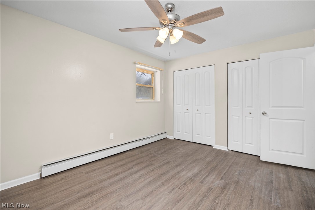 5382 Lee Road, Unit 102 Maple Heights, OH 44137 - Photo 21 of 25 Unfurnished bedroom featuring a baseboard radiator, multiple closets, wood finished floors, and ceiling fan