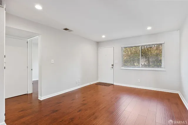 a view of an empty room with wooden floor and a window