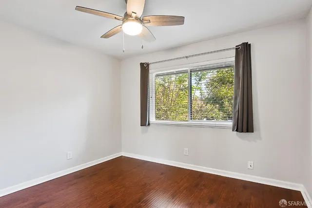 an empty room with wooden floor fan and windows