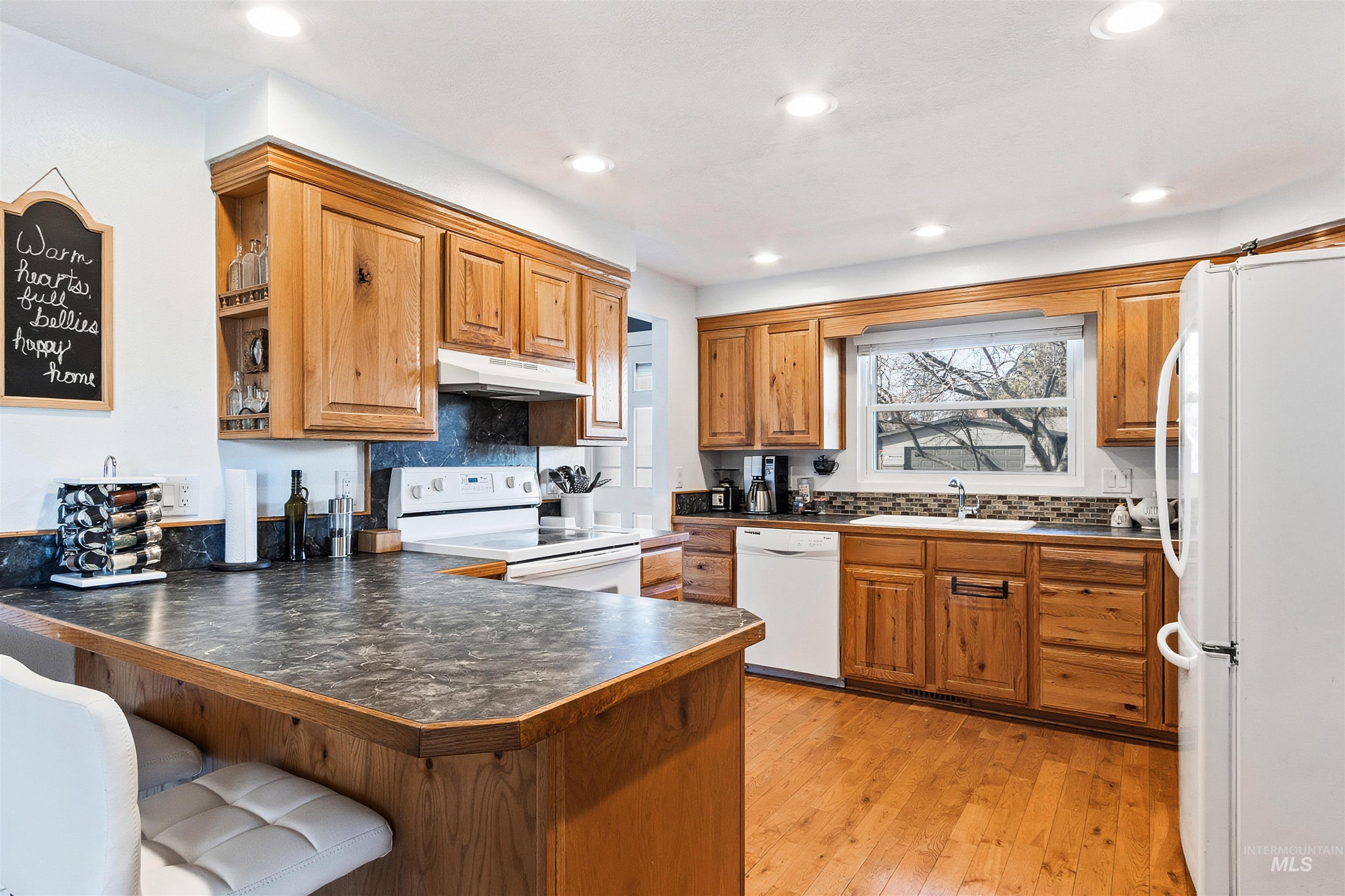 3844 North Patton Street Boise, ID 83704 - Photo 9 of 33 Kitchen with wood finish cabinets, dark countertops, white appliances, light wood finished floors, and backsplash