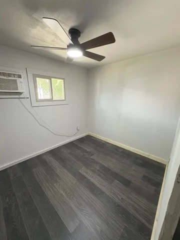 an empty room with wooden floor fan and windows
