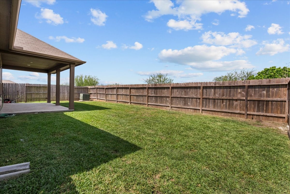 2320 Rosemary Street Rosenberg, TX 77469 - Photo 38 of 40 This photo showcases a spacious backyard with a well-maintained lawn and a wooden privacy fence. There's a covered patio area, perfect for outdoor gatherings. The space is open and inviting under a clear blue sky.