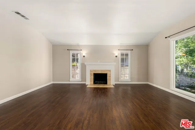 a view of an empty room with wooden floor fireplace and a window