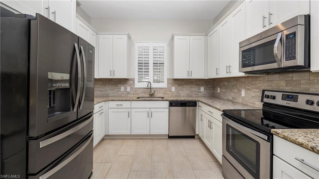 1238 Kendari Terrace Naples, FL 34113 - Photo 8 of 50 Kitchen featuring stainless steel appliances, white cabinetry, light stone counters, and backsplash