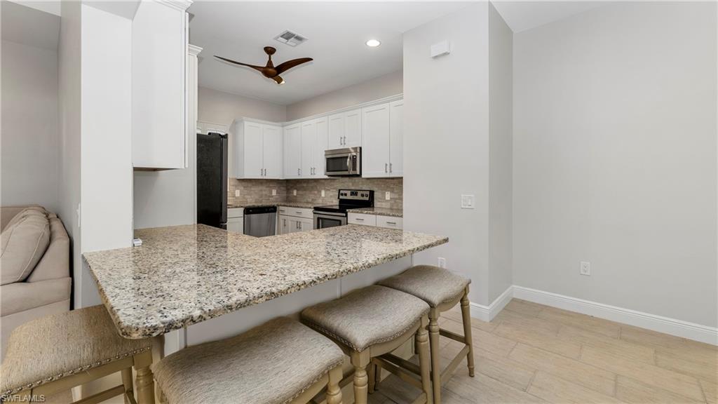 1238 Kendari Terrace Naples, FL 34113 - Photo 10 of 50 Kitchen featuring a peninsula, light stone countertops, tasteful backsplash, a breakfast bar area, and stainless steel appliances