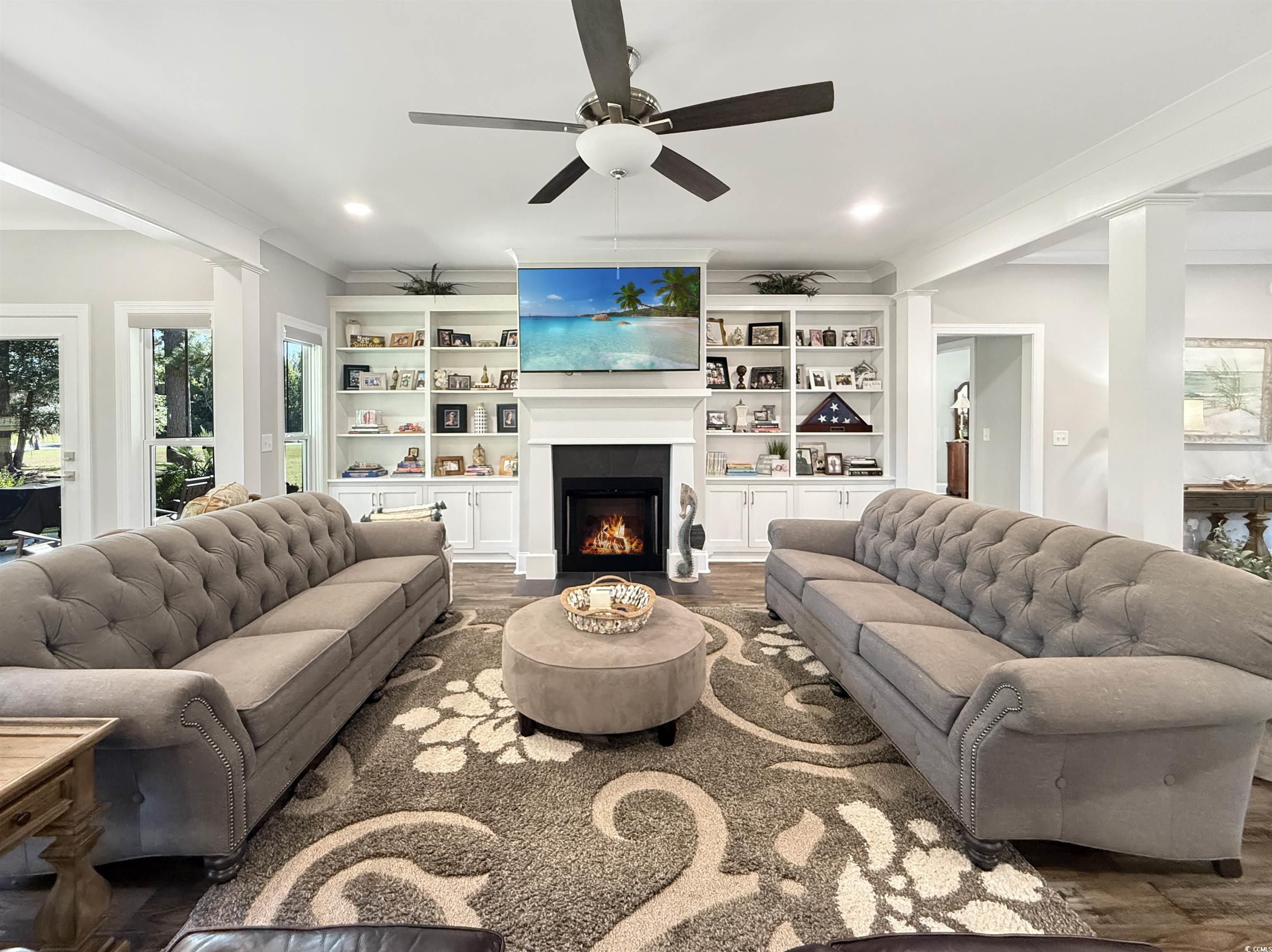 521 Oak Lawn Road Georgetown, SC 29440 - Photo 11 of 40 Living room featuring wood finished floors, a lit fireplace, a ceiling fan, built in shelves, and ornamental molding