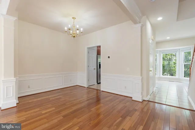 an empty room with wooden floor chandelier and windows