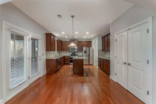 a kitchen with granite countertop wooden floors stainless steel appliances a sink and a center island