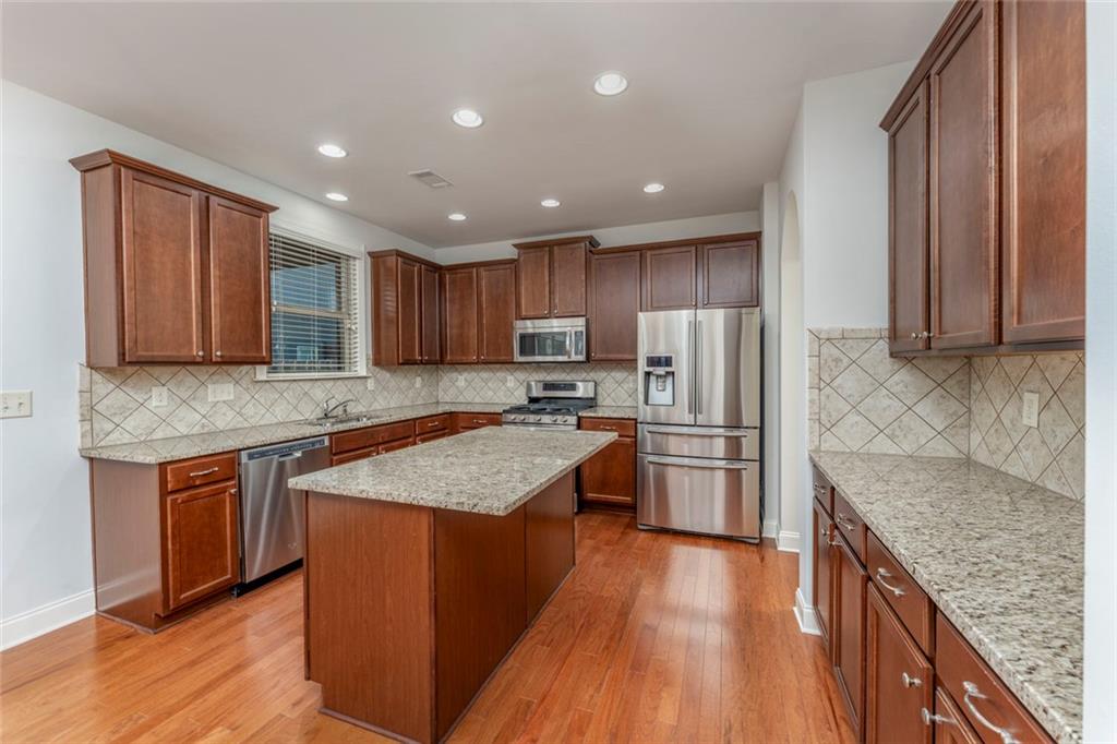 624 East Hampton Place Canton, GA 30115 - Photo 14 of 37 a kitchen with granite countertop wooden floors stainless steel appliances a sink and a center island