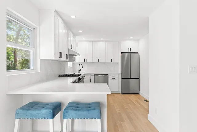 a kitchen with stainless steel appliances granite countertop a sink a refrigerator a stove a microwave oven with white cabinets and wooden floor