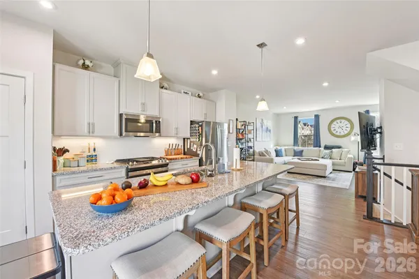 a kitchen with stainless steel appliances granite countertop a stove top oven a refrigerator a sink and white cabinets with wooden floor