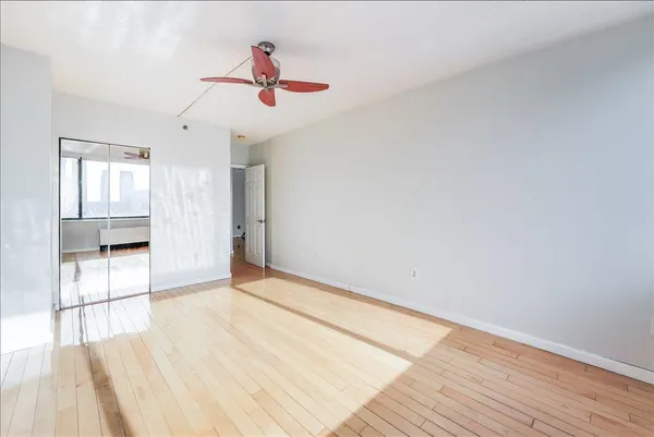 a view of an empty room with wooden floor and a ceiling fan