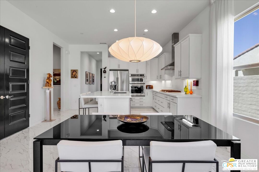 64 Claret Road Rancho Mirage, CA 92270 - Photo 17 of 30 a kitchen with a refrigerator a stove a sink and a dining table with chairs