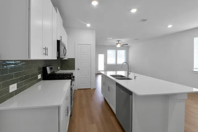 a large white kitchen with a sink and dishwasher a stove top oven with wooden floor