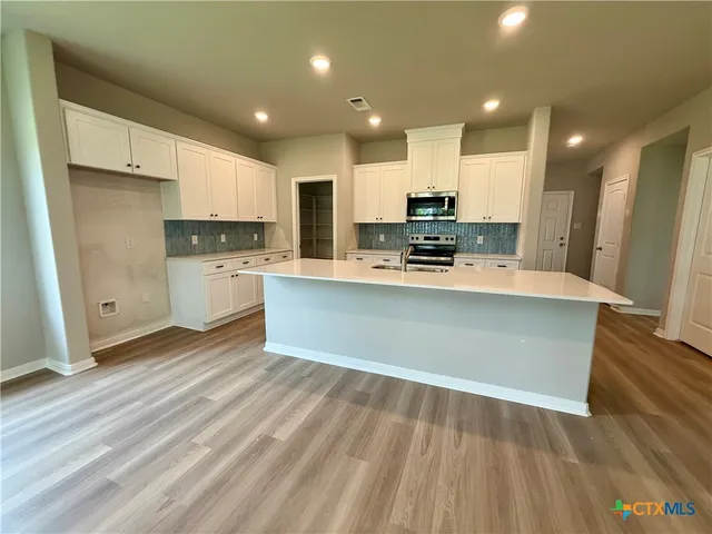 a large kitchen with stainless steel appliances a large counter top a stove and a refrigerator