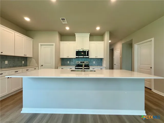 a large kitchen with kitchen island a stove a sink a refrigerator and white cabinets