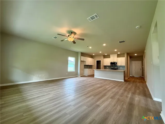 an empty room with wooden floor kitchen view and a window
