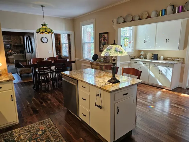 a kitchen with kitchen island granite countertop a stove a sink a dining table and chairs with wooden floor