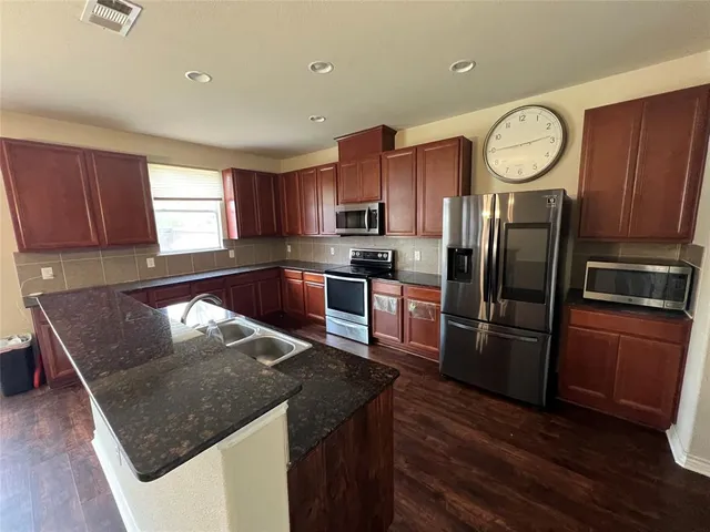 a kitchen with stainless steel appliances granite countertop a refrigerator a sink a stove a microwave and wooden cabinets