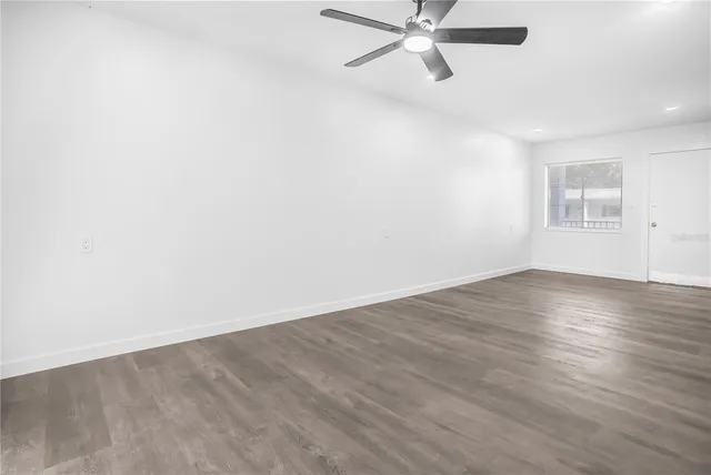 an empty room with wooden floor fan and windows