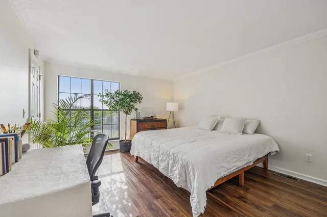 a bedroom with a bed table flowerpot and wooden floor