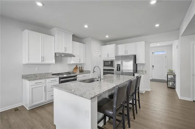 a kitchen with stainless steel appliances granite countertop a stove a sink a microwave a refrigerator and white cabinets with wooden floor