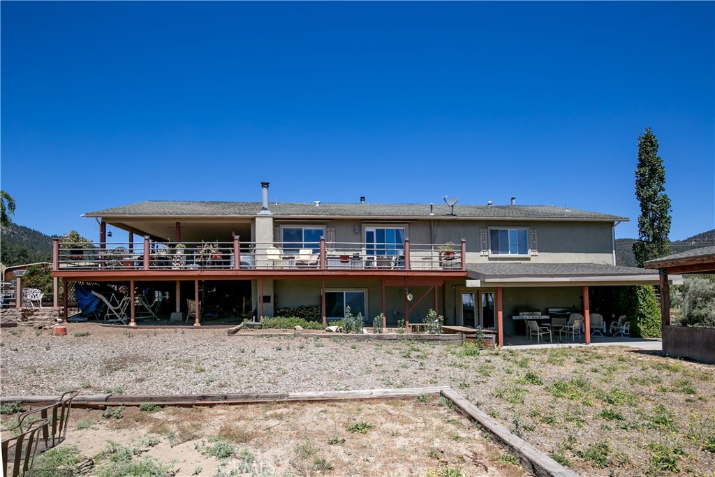 10960 Steinhoff Road Frazier Park, CA 93225 - Photo 16 of 46 A clear ground-level perspective of the home's rear exterior. This shot highlights the expansive upper-level wooden deck perfect for entertaining, a shaded lower patio area, and the open natural yard space set against a bright, clear blue sky.