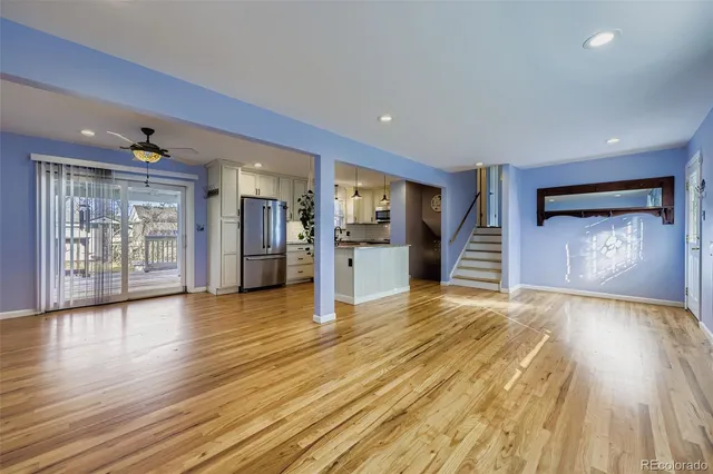 a view of an empty room with wooden floor and a kitchen