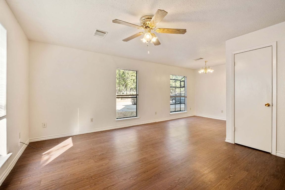 200 Concho Street, Unit B Lockhart, TX 78644 - Photo 2 of 13 Empty room featuring dark wood-type flooring, a ceiling fan, a chandelier, and a textured ceiling