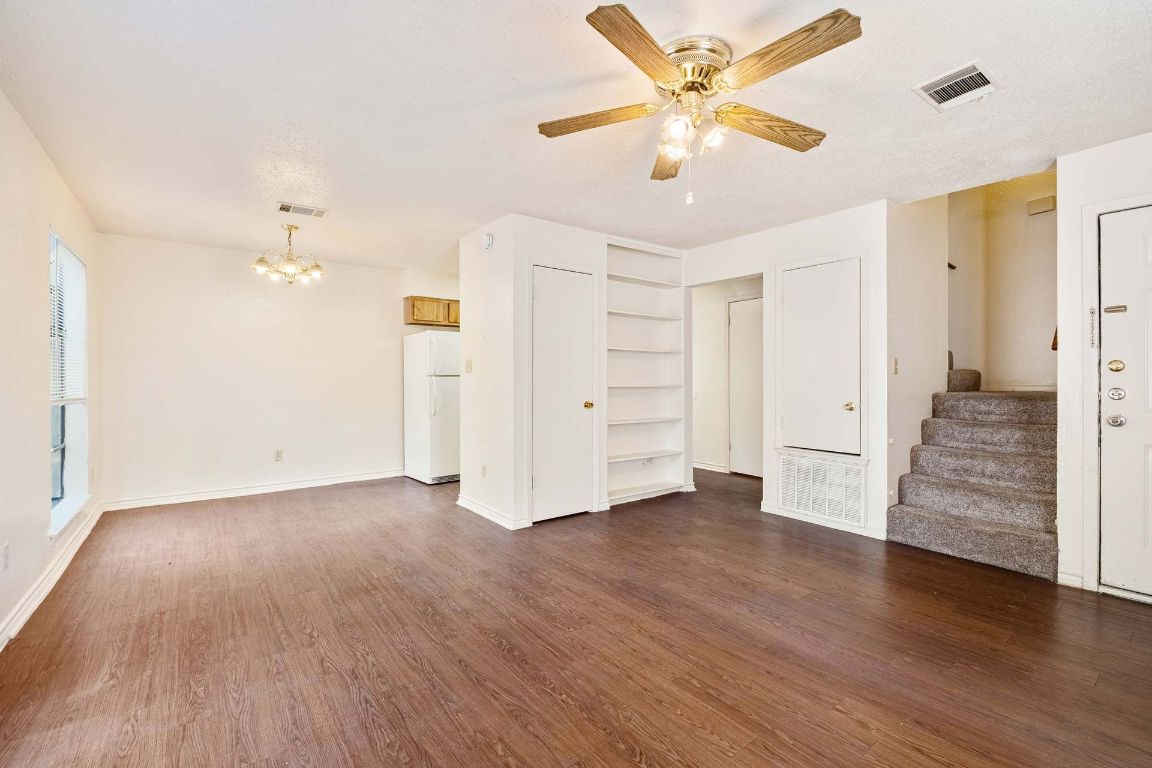 200 Concho Street, Unit B Lockhart, TX 78644 - Photo 3 of 13 Unfurnished living room with stairway, dark wood-type flooring, a chandelier, and ceiling fan