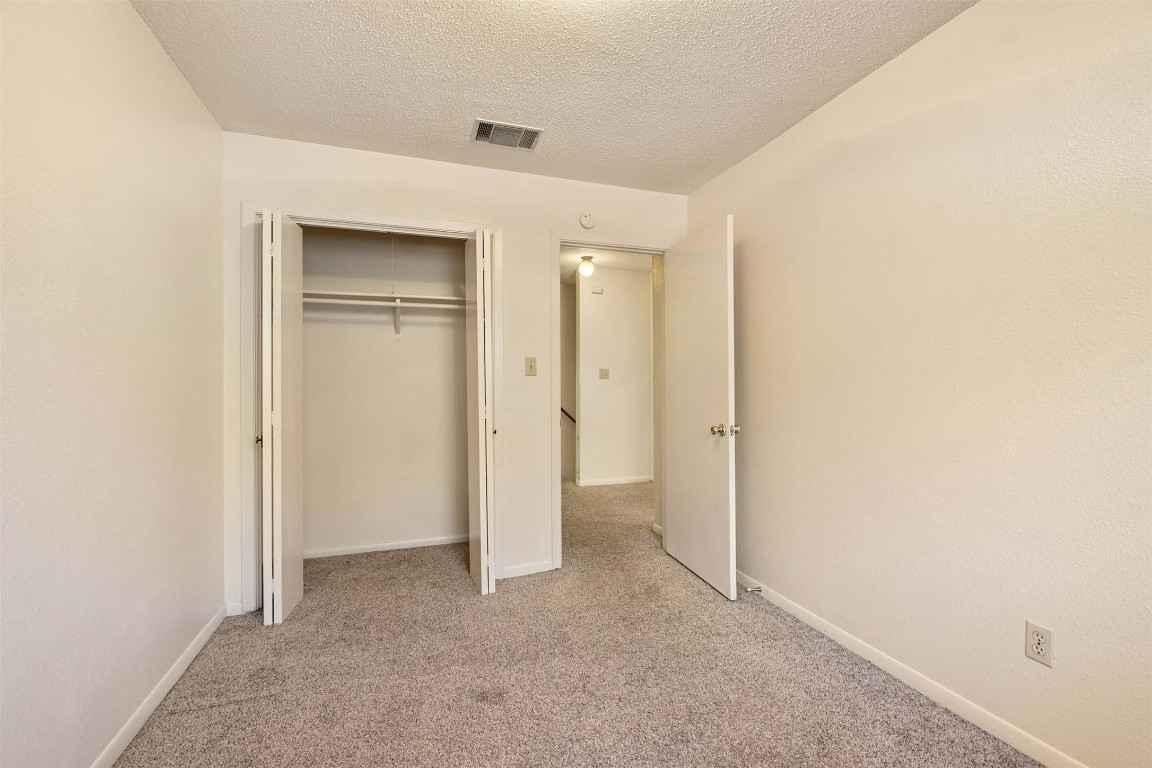 200 Concho Street, Unit B Lockhart, TX 78644 - Photo 10 of 13 Unfurnished bedroom featuring light carpet, a textured ceiling, and a closet