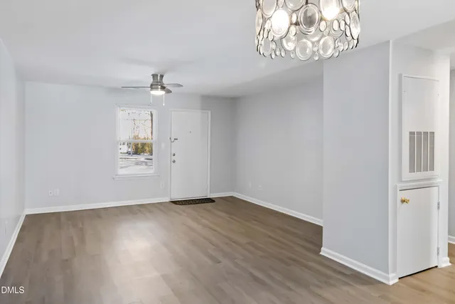 an empty room with wooden floor chandelier fan and windows