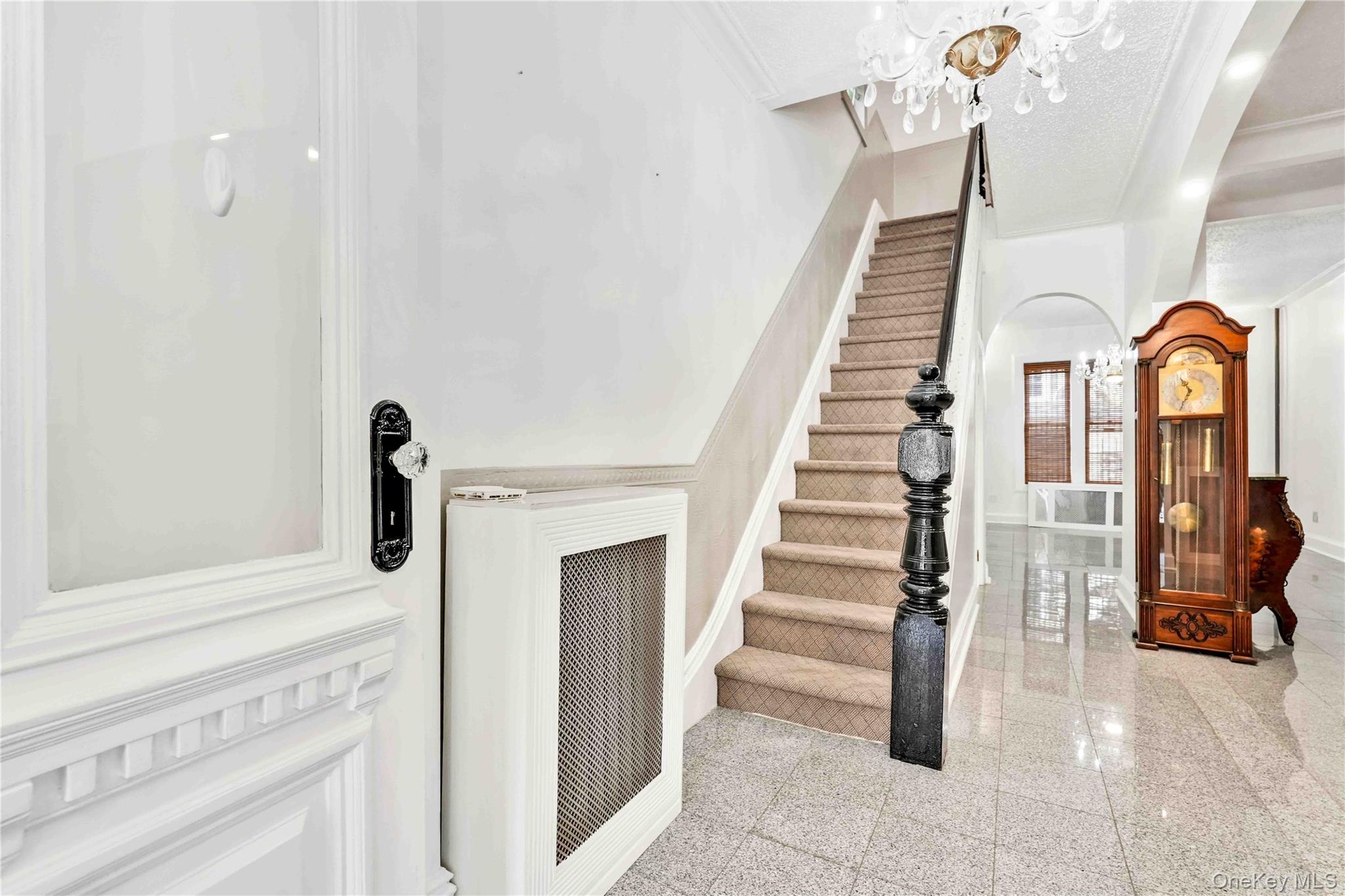 80-63 87th Road Queens, NY 11421 - Photo 28 of 50 Stairway featuring a chandelier, granite tiled floors, crown molding, radiator heating unit, and arched walkways