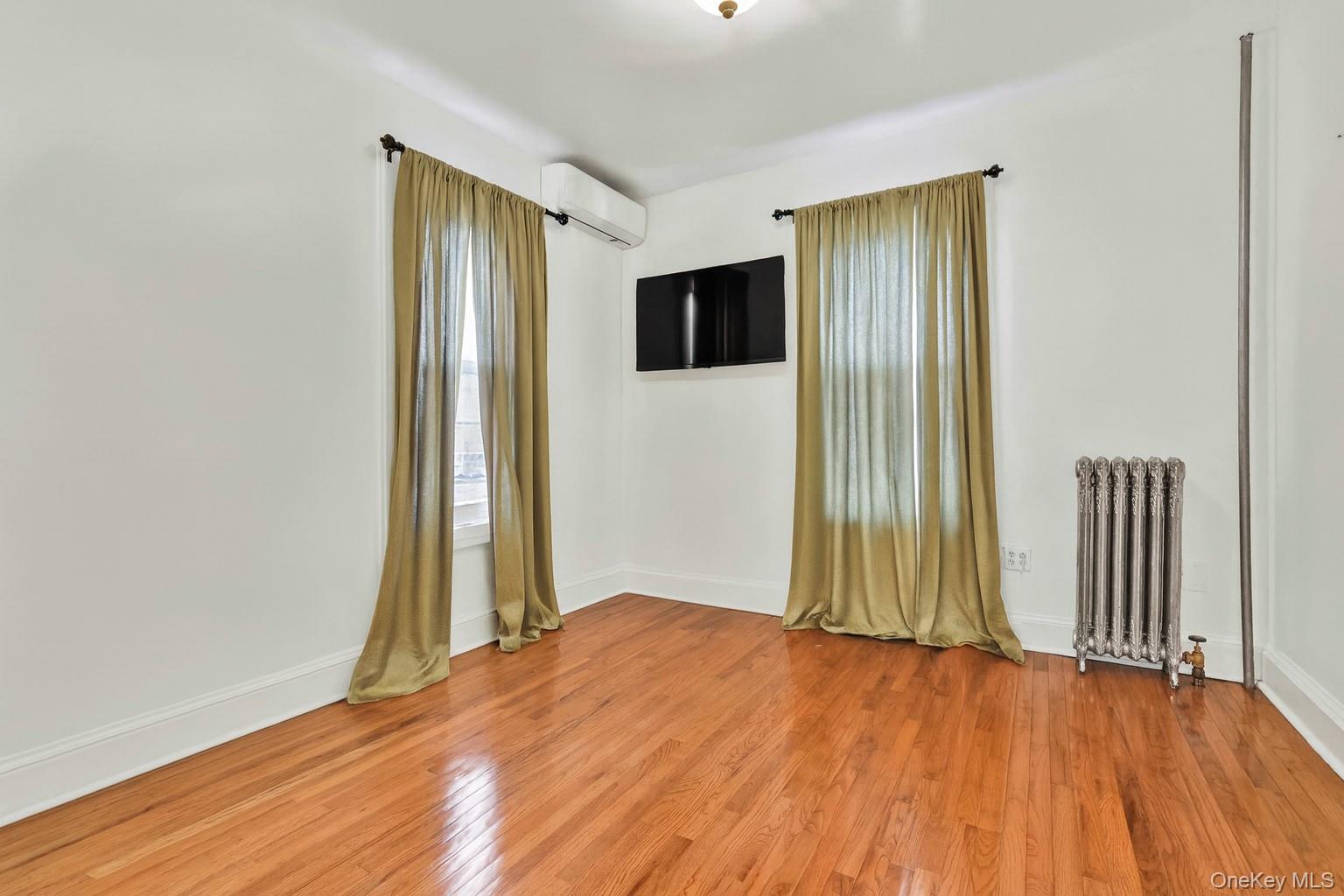80-63 87th Road Queens, NY 11421 - Photo 38 of 50 Empty bedroom featuring radiator heating unit, light wood-style floors, and a wall unit AC