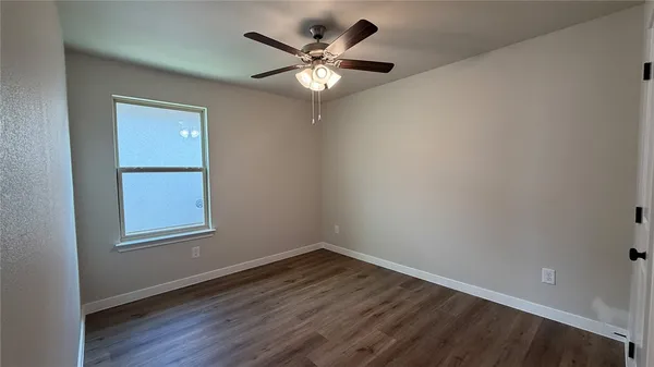 an empty room with wooden floor chandelier fan and windows