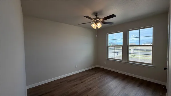 an empty room with wooden floor windows and fan