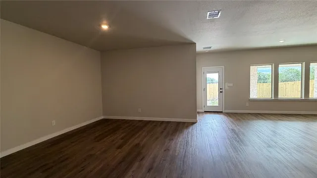 an empty room with wooden floor chandelier fan and windows