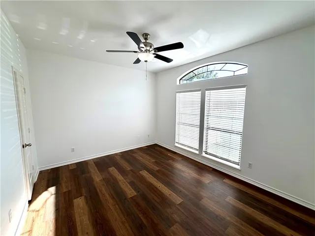 an empty room with wooden floor fan and windows