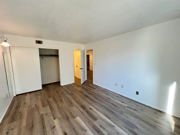 a view of an empty room with wooden floor and closet