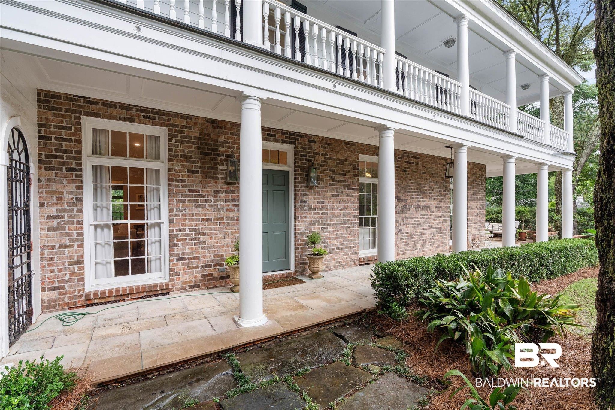 3908 Yester Place Mobile, AL 36608 - Photo 40 of 45 Brick facade featuring a columned veranda, stone patio, and a second-story balcony with balustrade railing